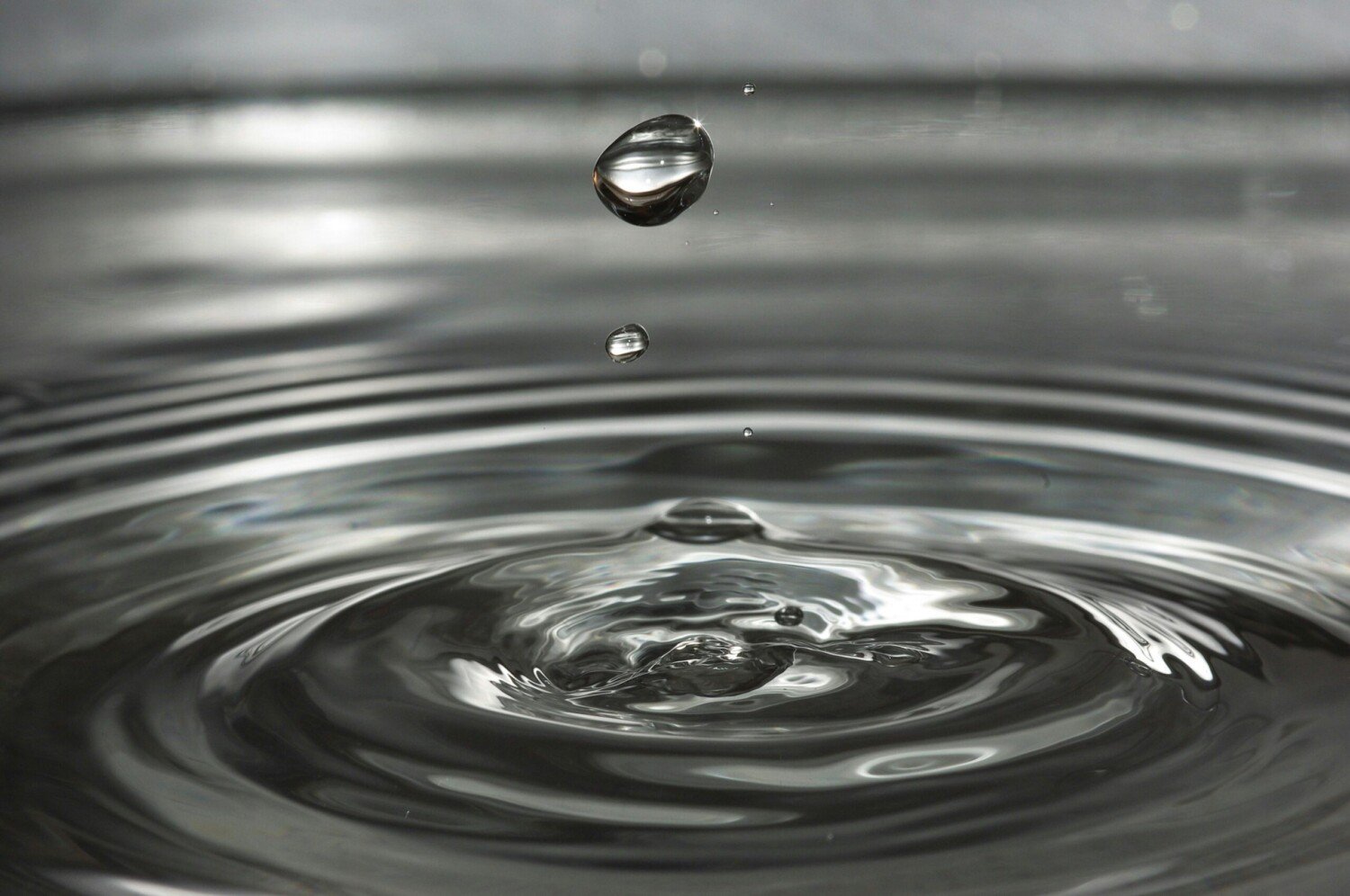Ein einzelner Wassertropfen fällt in die Oberfläche und erzeugt kreisförmige Wellen.